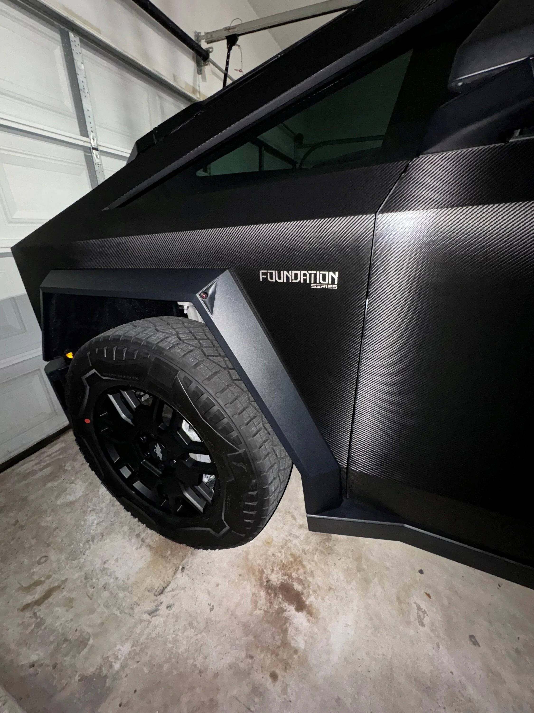 Tesla Cybertruck Carbon Fiber Black Wrap on my Cybertruck Drivers Side Tire and Foundation Badge (Home Garage)